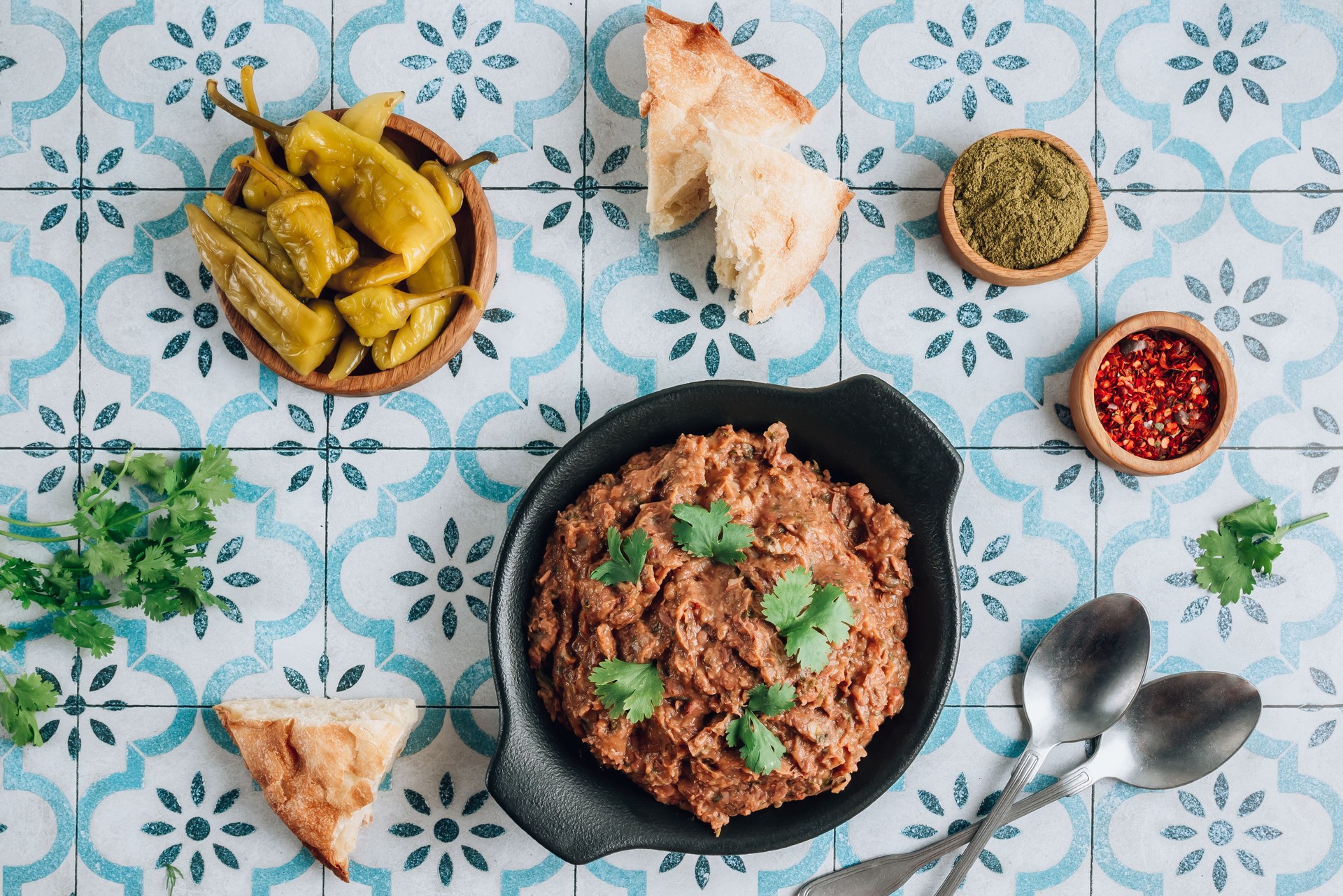 Mashed red bean with spices on blue tiles background. Traditional georgian dish lobio in black plate with bread and pickled hot peppers.